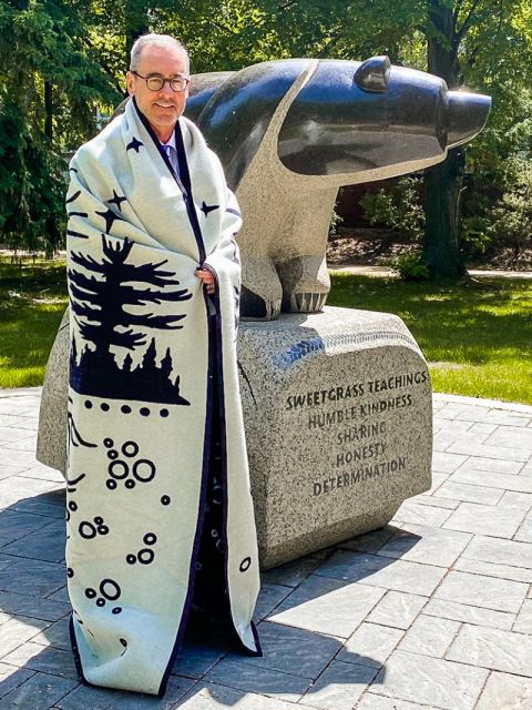 Bill Flanagan, former Dean of Queen’s Law, has begun his term as President of the University of Alberta. Standing beside the Sweetgrass Bear sculpture on the U of A campus, he is proudly wearing a gift from the Queen’s Law Dean’s Council and its Chair, David Sharpe, Law’95. The gift, a Manitobah Blanket by Pendleton Canada, reflects the commitment of Queen’s Law and the U of A to truth and reconciliation and indigenization. 