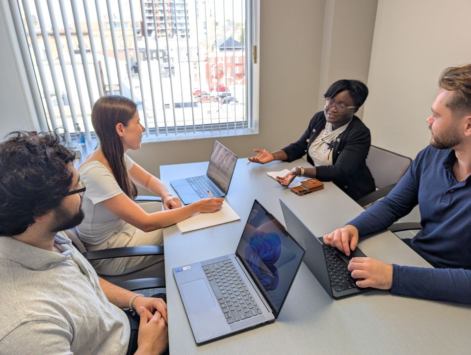 QBLC Director Tomi Adebiyi and student caseworkers discuss strategies for a client file in an interview room at the Queen’s Law Clinics.