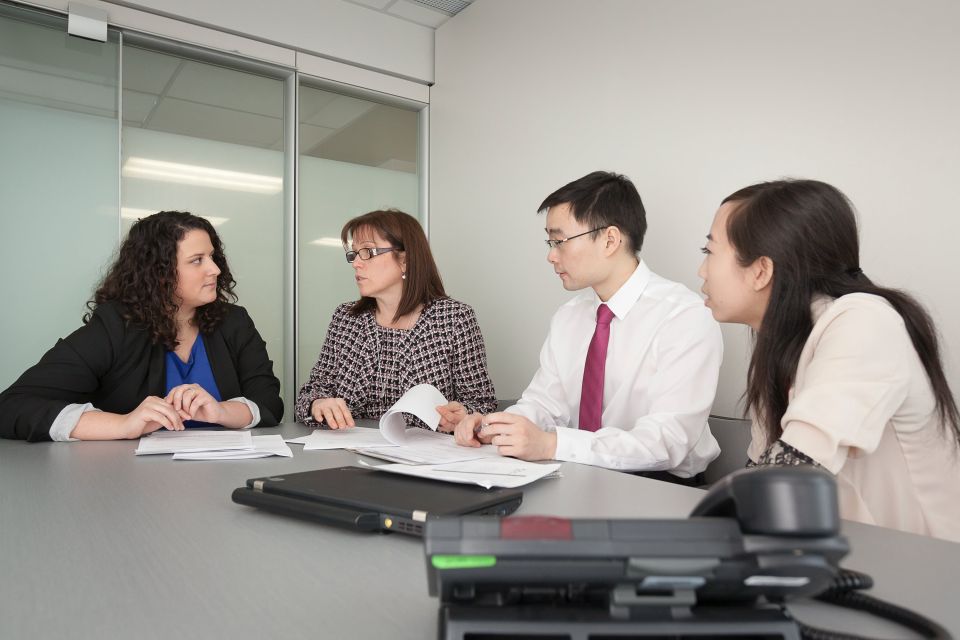 Four young people sit around a table with paper, a computer, and a telephone