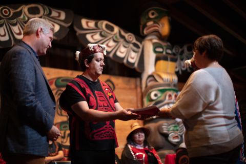 Kwakwaka’wakw and Coast Salish artist Carey Newman (Hayalthkin’geme), who created the Witness Blanket, presents the historic agreement he co-drafted with the Canadian Museum for Human Rights (CMHR) to CMHR Head of Collections Heather Bidzinski, while CMHR CEO and President John Young looks on. The agreement, allowing the museum to act as a caretaker of the legal entity blanket, was finalized in a ceremony on Oct. 16, 2019, at the K’ómoks Bighouse in the Comox Valley on Vancouver Island. (Photo by Media One)