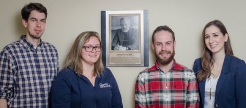 Queen's Law Journal editors Jason Paquette, Katrina van Kessel, Alexander Hinds and Jessica Toldo, all Law’16, stand beside the plaque commemorating Professor Bernie Adell outside the QLJ office.