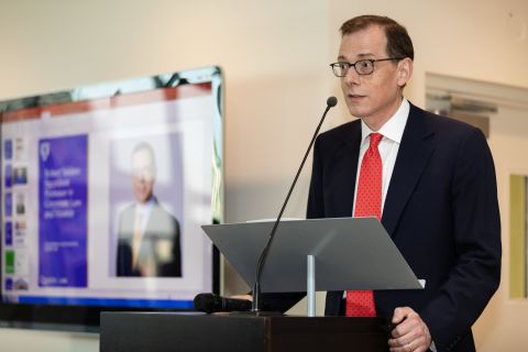 A person lectures in front of a digital screen