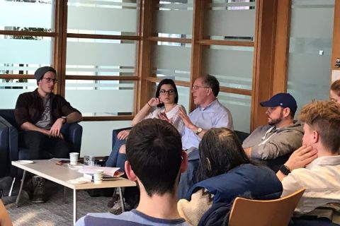 A professor speaks to a group of students gathered around a coffee table