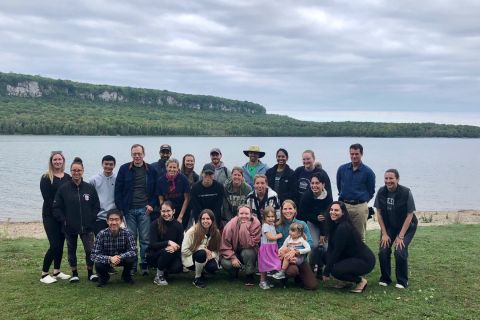 A photo of a group of people posing on grass in front of a lake
