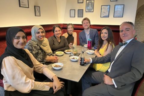 A photo of several people sitting around a table with dishes of food on it
