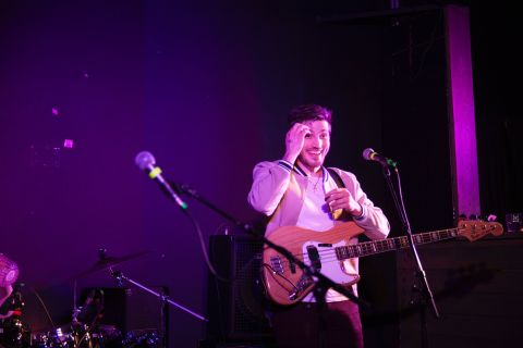 A young person stands behind a microphone with a bass guitar